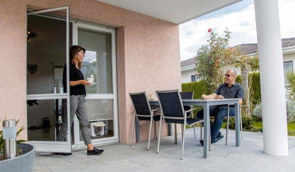 Frau läuft durch eine Fliegengitter Pendeltür auf die Terrasse und trägt eine Kaffeetasse in der Hand.